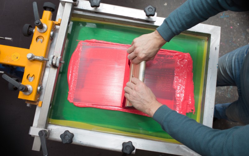 operaio che pressa l’inchiostro sul telaio con lo spremitore per la stampa in serigrafia